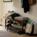 Banco sapateira e ganchos na entrada de um apartamento, com bolsa e calçados de uso diário organizados em uma drop zone simples.