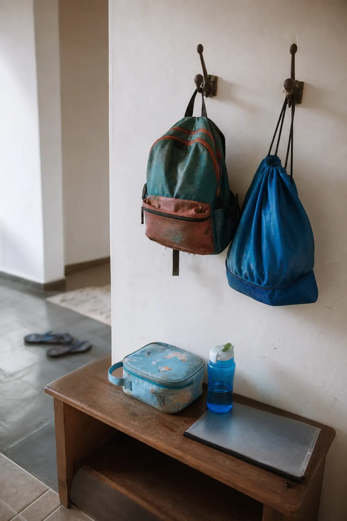 Ponto de transição pós-escola com mochila, bolsa de atividade, lancheira e recados organizados.