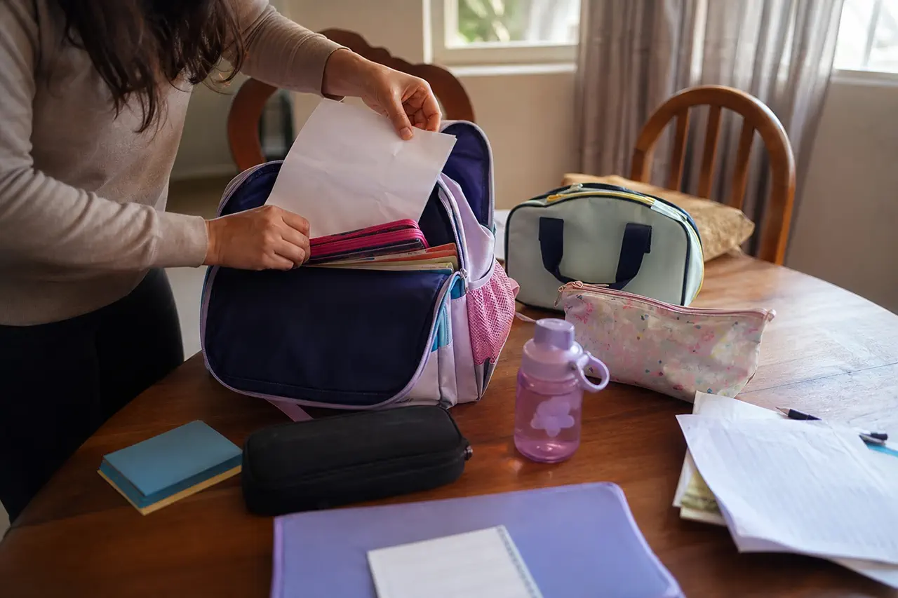 Checklist visual simples de pós-escola ao lado de ganchos com mochila e bolsa de atividade já prontas para a rotina da tarde.